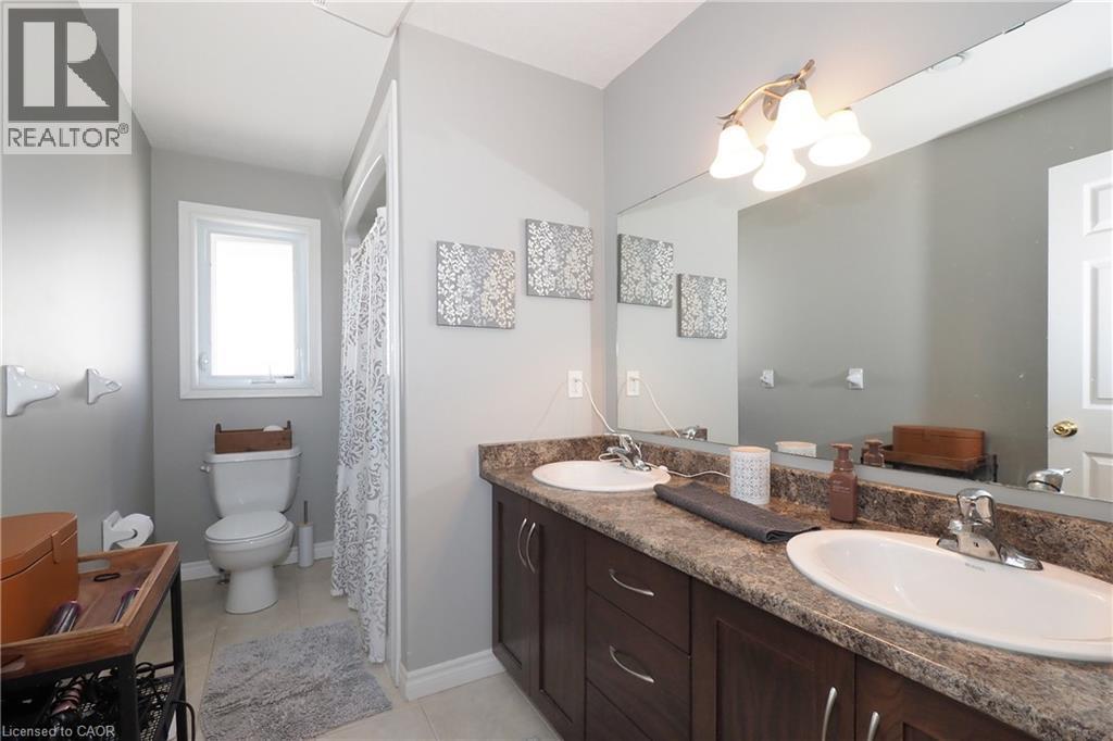 Double vanity with integrated sinks, wood-finish cabinetry, and a full-width mirror with an attached vanity light fixture - 1200 Dunbar Road, Cambridge, ON