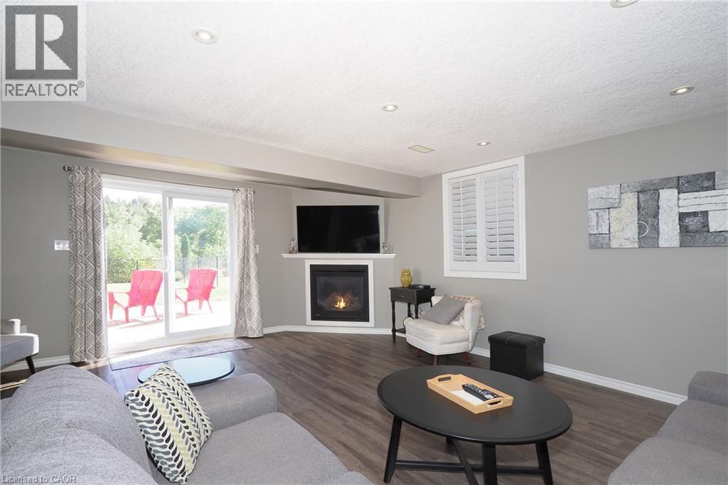 Fireplace with mantel, sliding glass door to exterior, window with plantation shutters, wood-finish flooring, and recessed lighting - 1200 Dunbar Road, Cambridge, ON