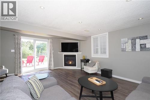 Fireplace with mantel, sliding glass door to exterior, window with plantation shutters, wood-finish flooring, and recessed lighting - 1200 Dunbar Road, Cambridge, ON 