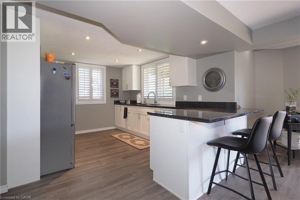 Kitchen featuring dark stone countertops, white cabinetry, wood-finish flooring, and recessed ceiling lighting - 1200 Dunbar Road, Cambridge, ON