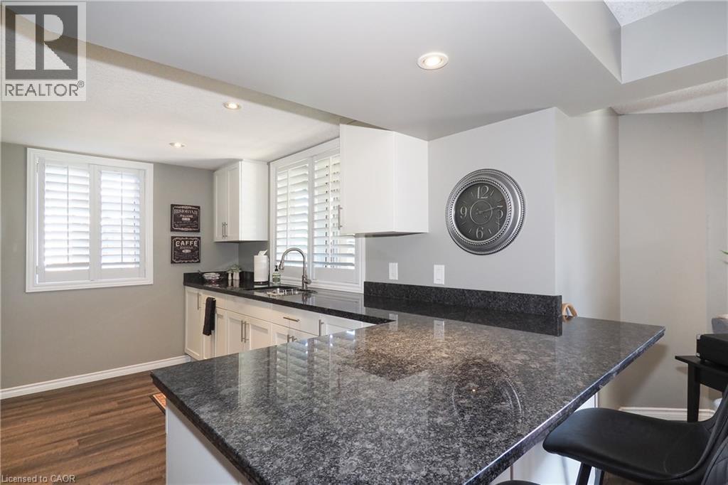Kitchen featuring dark speckled countertops, white cabinetry, undermount sink, and wood-finish flooring - 1200 Dunbar Road, Cambridge, ON
