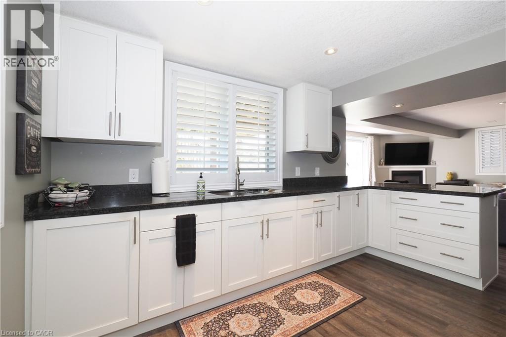 White shaker-style cabinetry, dark countertops, wood-finish flooring, recessed lighting, and a kitchen sink with a window - 1200 Dunbar Road, Cambridge, ON
