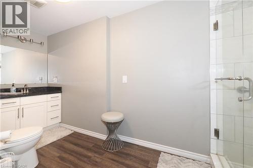 Modern bathroom featuring a glass-enclosed shower, wood-finish flooring, white vanity with stone countertop, and an elongated toilet - 1200 Dunbar Road, Cambridge, ON 