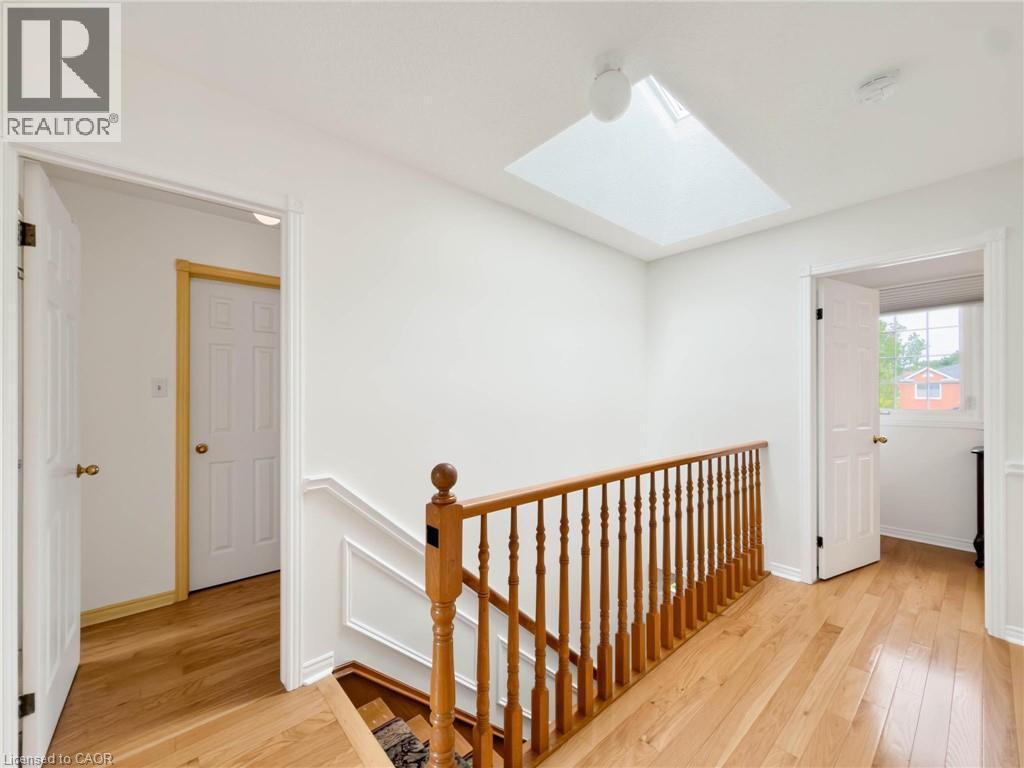 Hardwood flooring and a skylight illuminate this upper-level hallway, featuring a wood spindle railing and white trim details - 1236 Thorpe Road, Burlington, ON