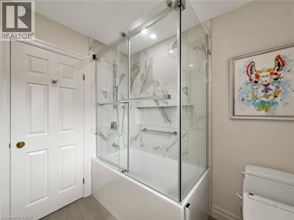 Tub and shower combination with glass enclosure, marble-patterned tile, and recessed shelving - 1236 Thorpe Road, Burlington, ON