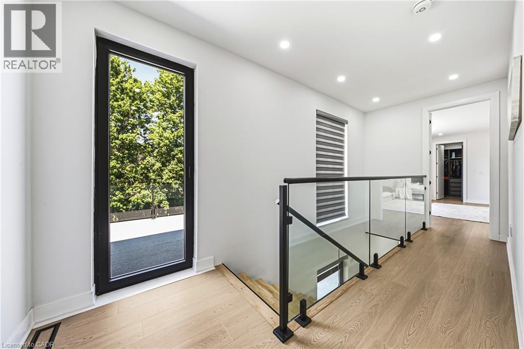 Wood-finish flooring throughout, modern glass and metal railing, recessed ceiling lighting, and a full-height window with dark framing - 4511 Guelph Line, Burlington, ON
