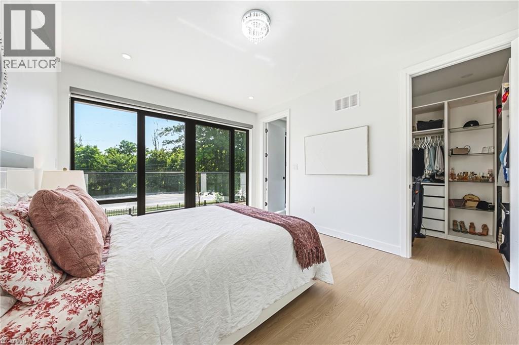 Expansive sliding glass doors, light wood-finish flooring, a contemporary ceiling light fixture, and a built-in closet system - 4511 Guelph Line, Burlington, ON