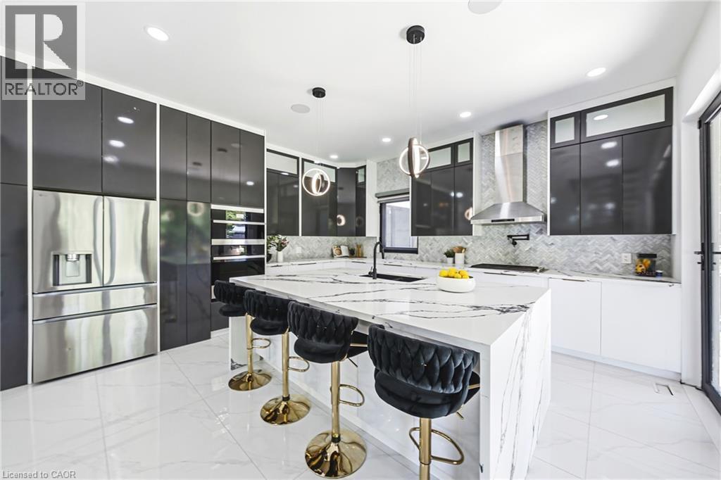 Waterfall island with integrated sink, stainless steel appliances, herringbone backsplash, recessed lighting, and black cabinetry - 4511 Guelph Line, Burlington, ON