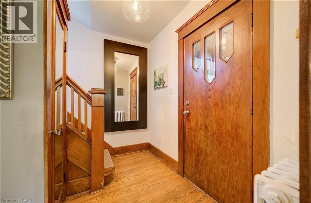 Wood-finish flooring, wood staircase with balusters, wood door with decorative glass inserts, and a wall-mounted mirror - 90 Brock Street, Kitchener, ON