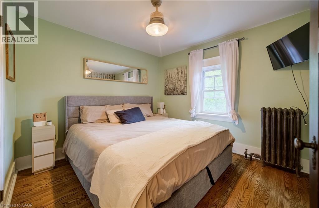 Hardwood flooring, painted walls, ceiling-mounted light fixture, window with trim, and a radiator - 90 Brock Street, Kitchener, ON