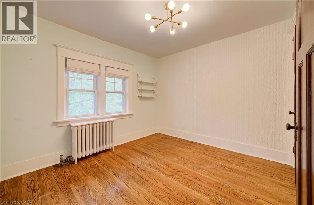 Hardwood flooring throughout, large windows with white trim, a decorative radiator, and a contemporary ceiling light fixture - 90 Brock Street, Kitchener, ON