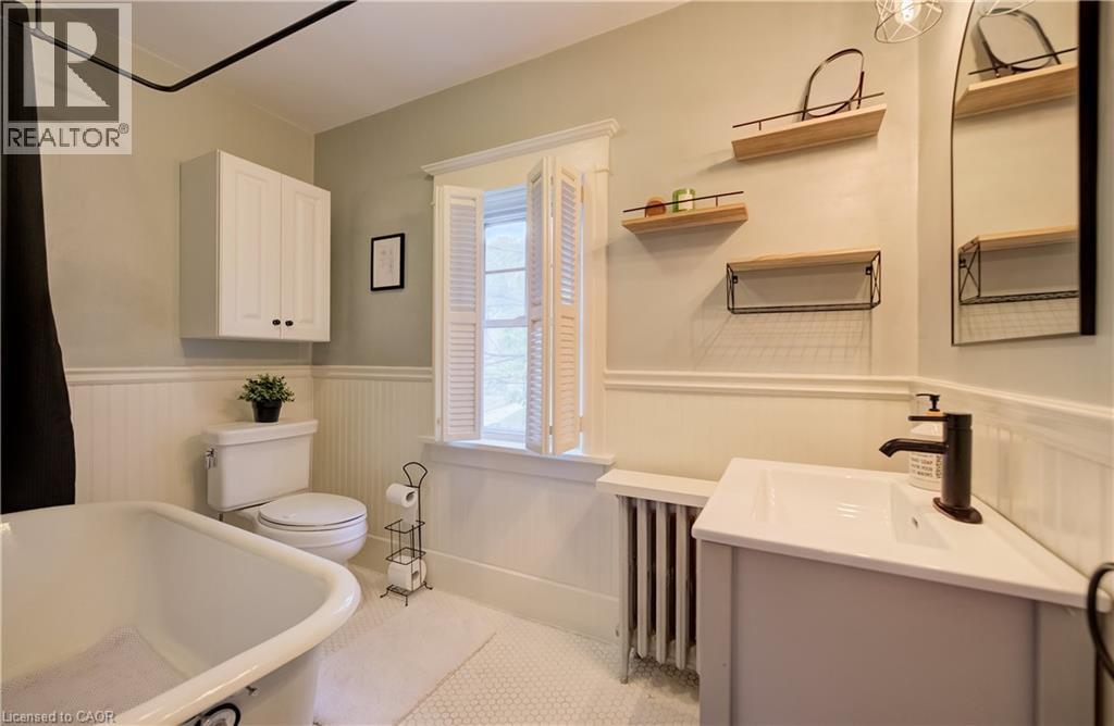 Bathroom featuring a freestanding tub, white beadboard wainscoting, wall-mounted storage cabinet, and a single vanity with a black faucet - 90 Brock Street, Kitchener, ON