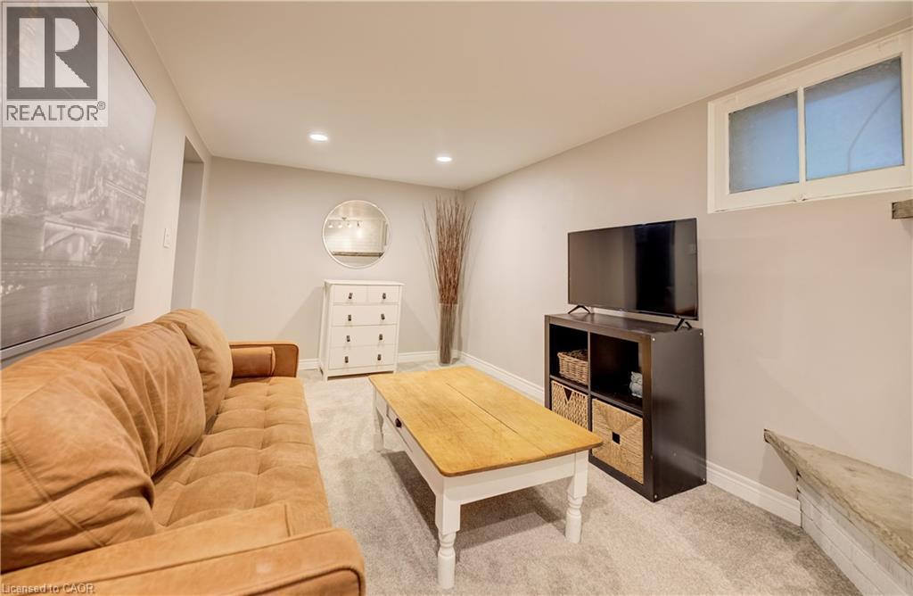 Finished basement recreation room featuring a cognac leather sectional sofa, wood-finish coffee table, media console with open shelving, recessed ceiling lighting, carpeted flooring, and a high window - 90 Brock Street, Kitchener, ON