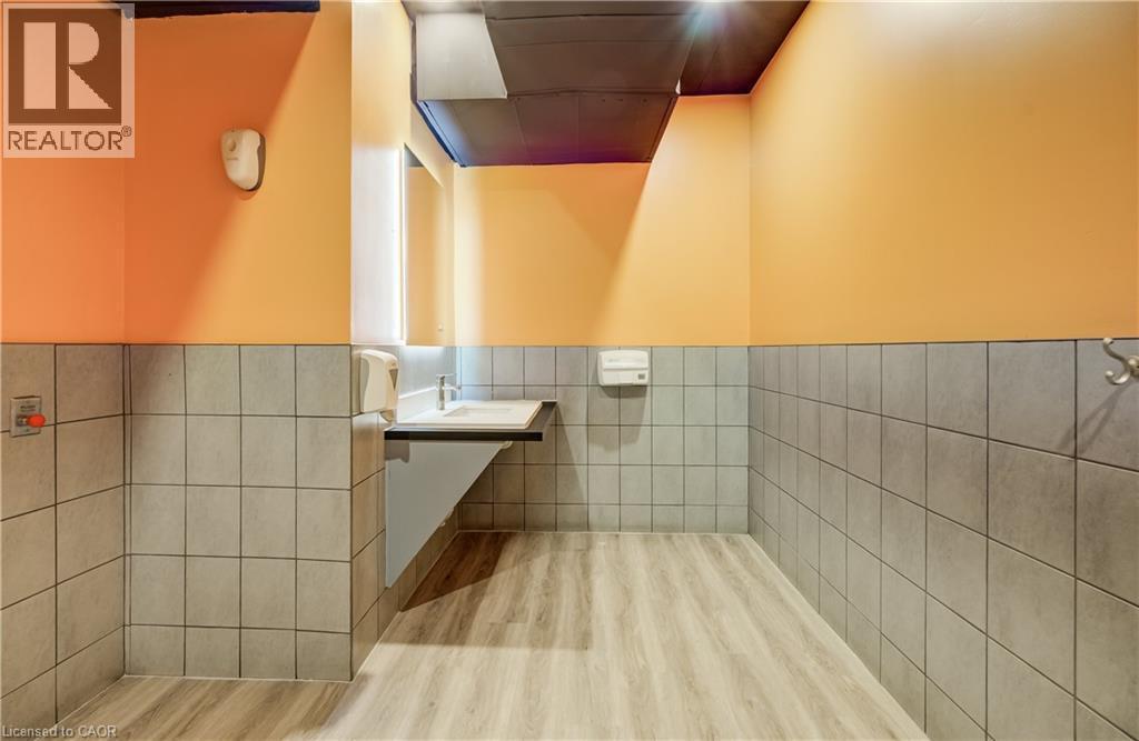 Wood-finish flooring, half-wall gray tiling, wall-mounted sink with chrome faucet, light orange painted walls, and dark ceiling - 1118 King Street E, Cambridge, ON