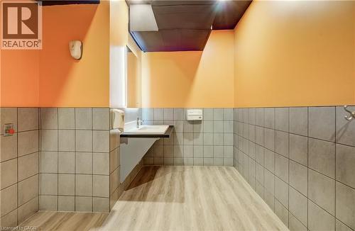 Wood-finish flooring, half-wall gray tiling, wall-mounted sink with chrome faucet, light orange painted walls, and dark ceiling - 1118 King Street E, Cambridge, ON 