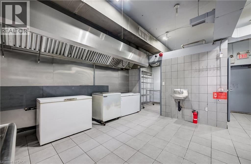 Commercial-grade kitchen space featuring a stainless steel exhaust hood, tile flooring, and fully tiled walls - 1118 King Street E, Cambridge, ON