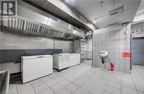 Commercial-grade kitchen space featuring a stainless steel exhaust hood, tile flooring, and fully tiled walls - 1118 King Street E, Cambridge, ON 