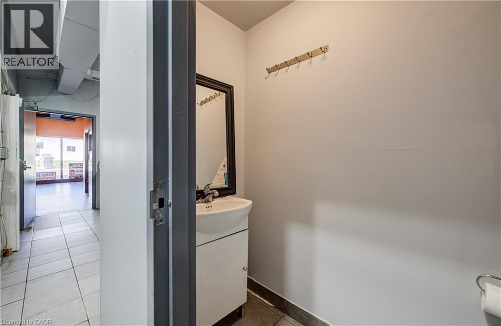 Restroom featuring a wall-mounted mirror, single basin sink with white vanity, and ceramic tile flooring - 1118 King Street E, Cambridge, ON