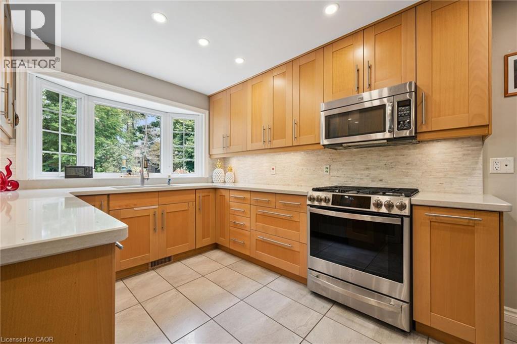 Light-toned wood cabinetry with stainless steel hardware, a stainless steel range and microwave, light-toned countertops, and a bay window - 334 Coleridge Drive, Waterloo, ON