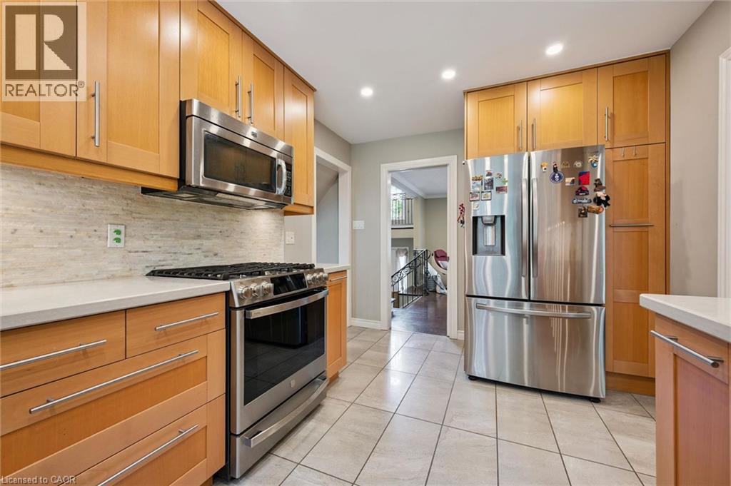 Light wood-finish cabinetry with stainless steel hardware, stainless steel appliances, light-toned backsplash, white countertops, and tiled flooring - 334 Coleridge Drive, Waterloo, ON