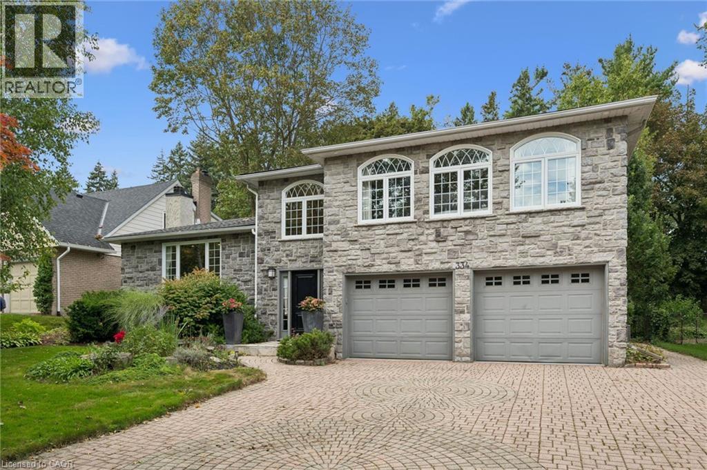Stone facade with arched windows, an intricate paver driveway, and an attached two-car garage - 334 Coleridge Drive, Waterloo, ON