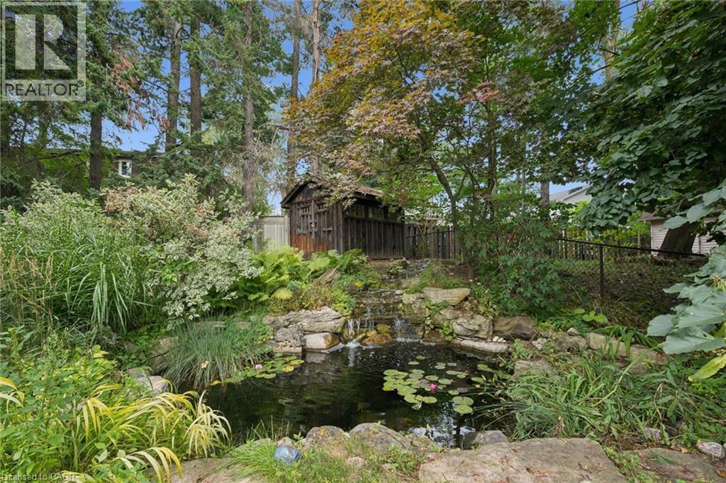 Water feature with rock accents, mature trees, dense foliage, and a wooden shed - 334 Coleridge Drive, Waterloo, ON