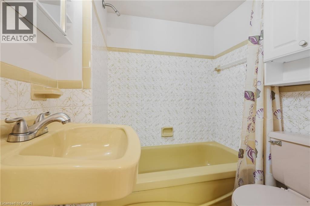 Built-in bathtub, pedestal sink, wall-mounted showerhead, and white wall cabinets - 137 Picton Street E, Hamilton, ON
