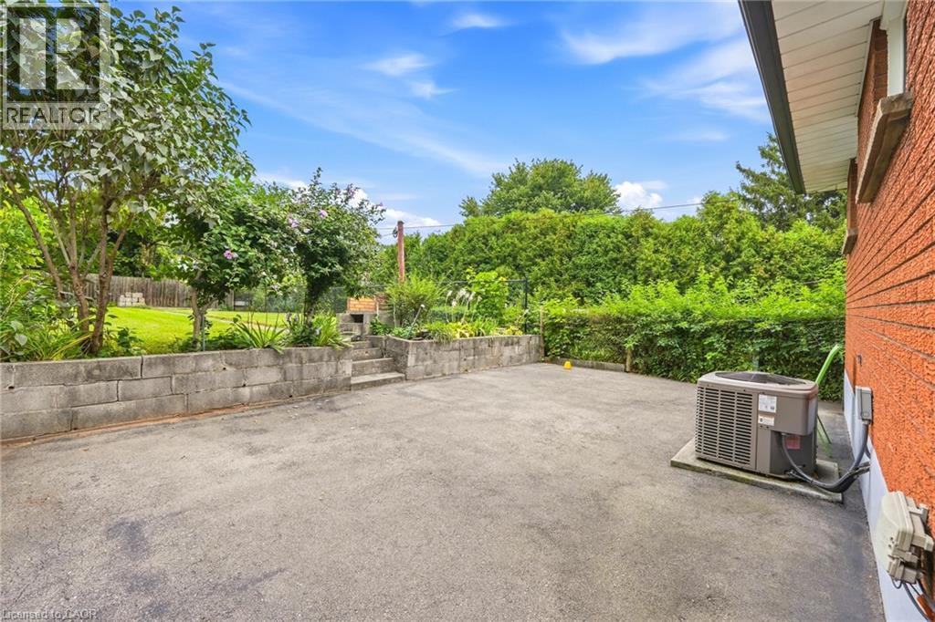 Paved patio area featuring a concrete block retaining wall, integrated steps, and mature landscaping - 137 Picton Street E, Hamilton, ON