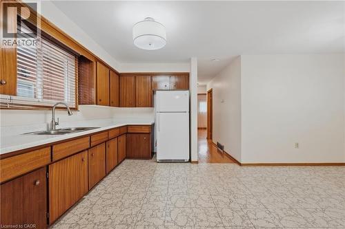 Kitchen featuring wood-finish cabinetry, a double basin stainless steel sink with a gooseneck faucet, a white refrigerator, and patterned floor tile - 137 Picton Street E, Hamilton, ON 