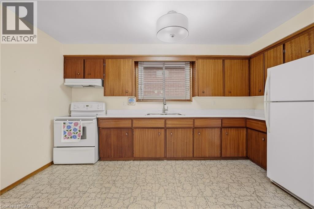 L-shaped kitchen featuring wood-finish cabinetry, white countertops, and white appliances - 137 Picton Street E, Hamilton, ON