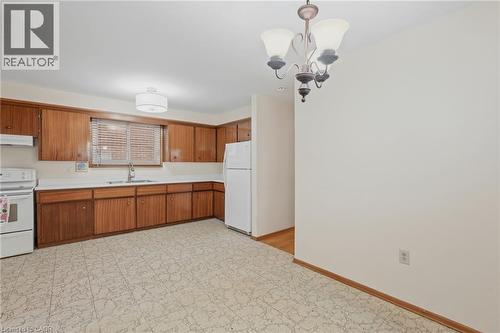 Kitchen area featuring wood cabinetry, white countertops, a stainless steel sink, and white appliances - 137 Picton Street E, Hamilton, ON 
