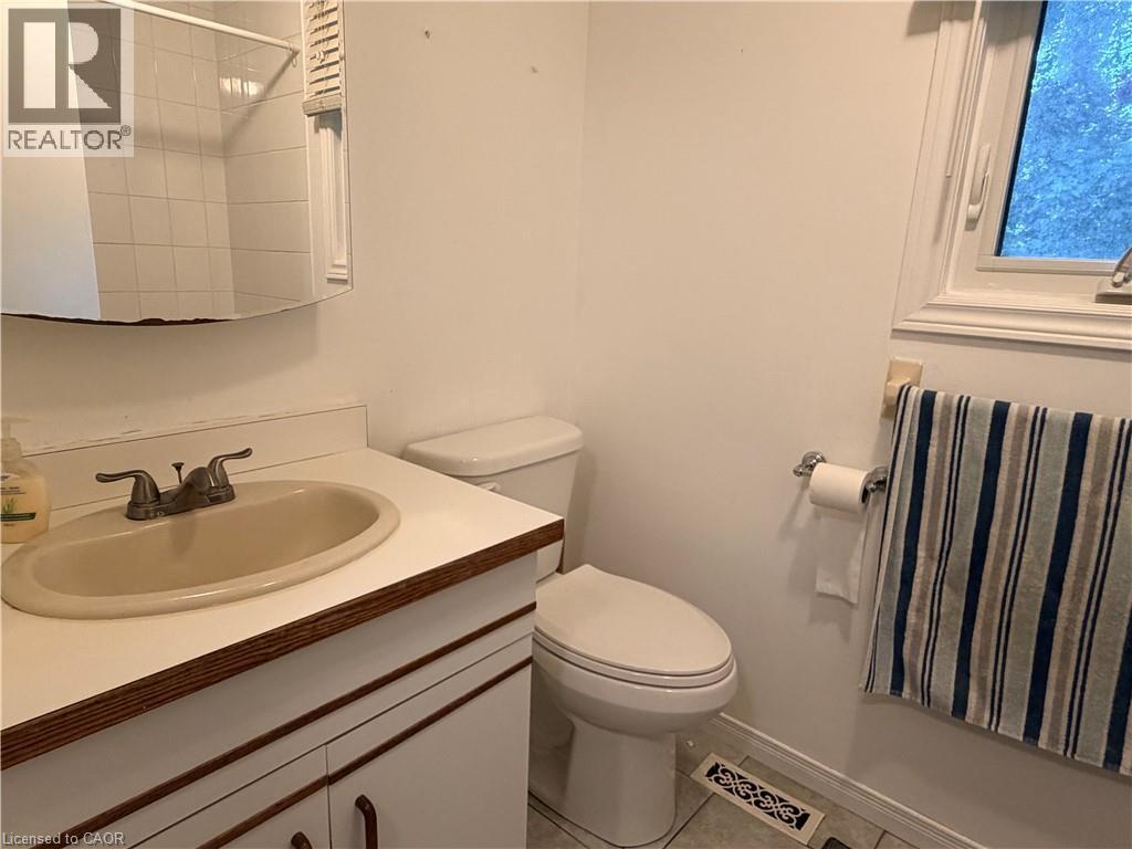 Vanity with integrated sink, wall-mounted mirror, white commode, tiled shower enclosure, and window - 450 Bridge Street W, Waterloo, ON