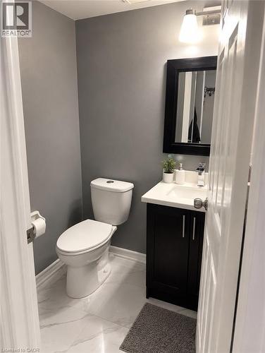 White tile flooring with subtle veining, dark vanity with a white countertop, and a wall-mounted light fixture - 125 Fairgreen Close, Cambridge, ON 