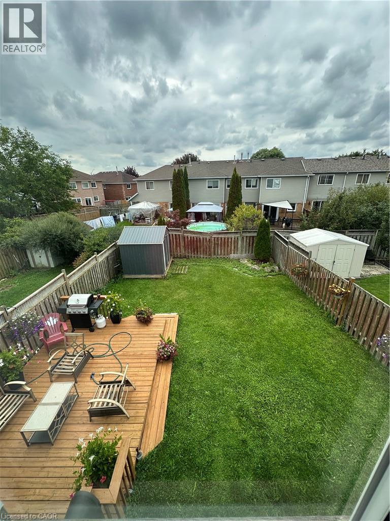 Expansive backyard featuring a wood deck, green lawn, two storage sheds, and wood fencing - 125 Fairgreen Close, Cambridge, ON