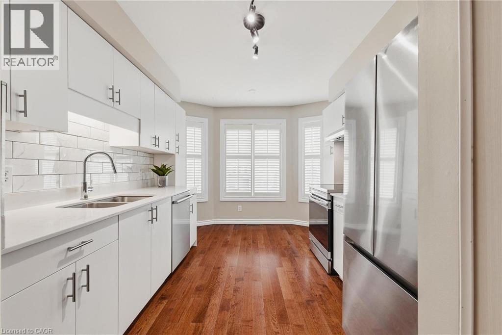 Kitchen featuring white cabinetry, subway tile backsplash, stainless steel appliances, wood-finish flooring, and a bay window with plantation shutters - 245 Bishop Street S Unit# 31, Cambridge, ON