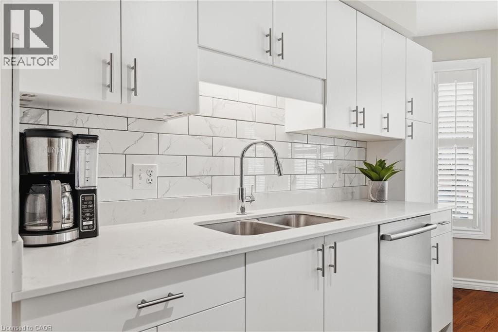 Kitchen featuring white shaker cabinetry with brushed nickel hardware, white stone countertops, a subway tile backsplash with subtle veining, a stainless steel double-basin sink with a gooseneck fauce - 245 Bishop Street S Unit# 31, Cambridge, ON
