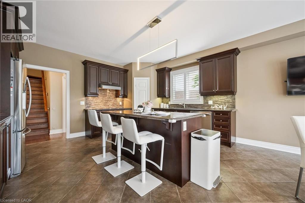 Kitchen featuring dark wood cabinetry, a central island with seating, stainless steel appliances, and tile flooring - 517 Topper Woods Crescent, Kitchener, ON