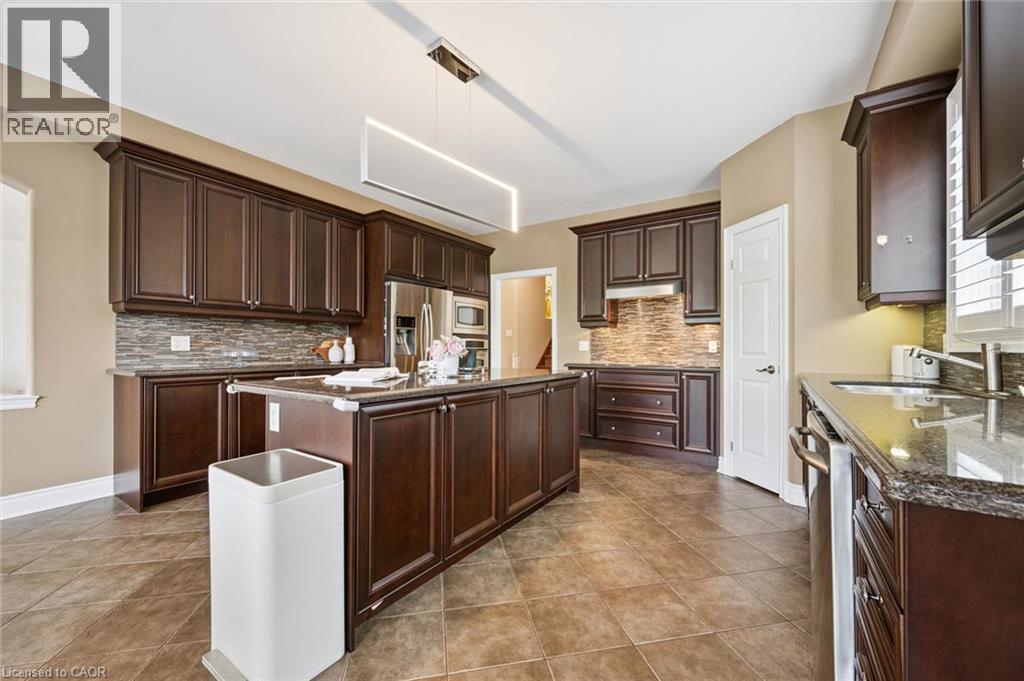 Kitchen featuring dark wood cabinetry, a central island with countertop space, stainless steel appliances, a tile backsplash, and tile flooring - 517 Topper Woods Crescent, Kitchener, ON