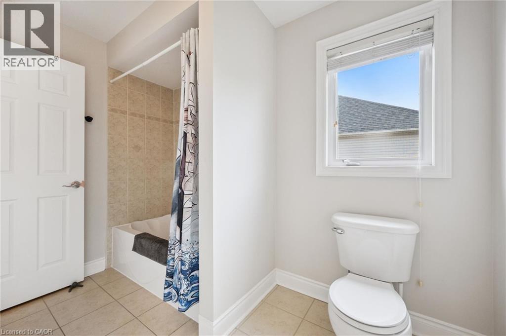 White paneled door, tile flooring, tiled shower surround, built-in bathtub, and a window with blinds - 517 Topper Woods Crescent, Kitchener, ON