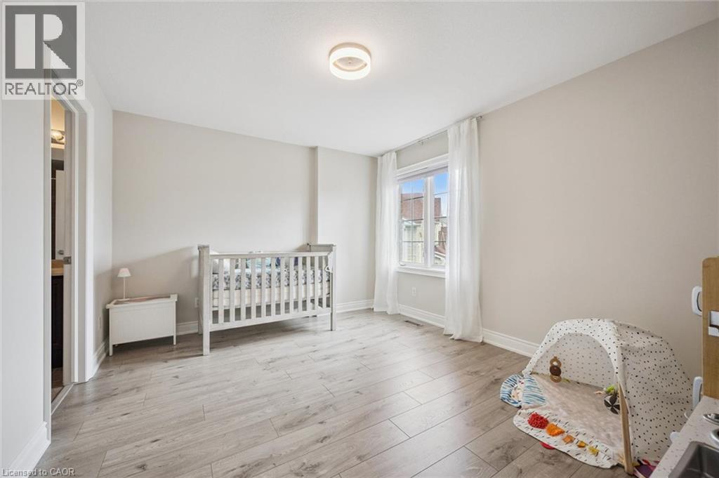 Light wood-finish flooring, neutral wall tones, window with natural light, modern ceiling light fixture, and white trim - 517 Topper Woods Crescent, Kitchener, ON