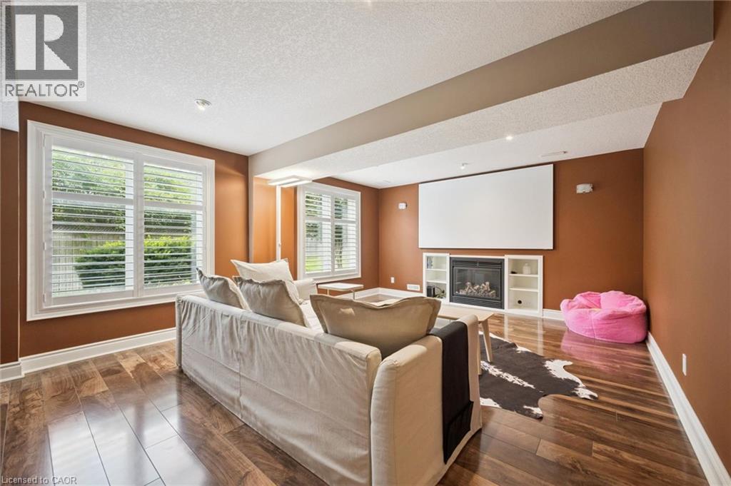 Spacious room featuring wood-finish flooring, multiple windows with white plantation shutters, a built-in fireplace with shelving, and a large projection screen - 517 Topper Woods Crescent, Kitchener, ON