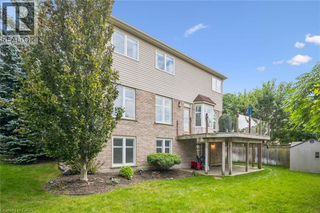 Expansive rear yard featuring a wooden deck with glass railing, a bay window, and a storage shed - 517 Topper Woods Crescent, Kitchener, ON