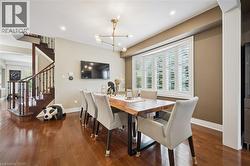 Rich wood-finish flooring, a contemporary chandelier, and a bay window with plantation shutters define this space -
