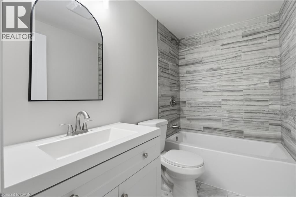 White vanity with integrated sink, brushed nickel faucet, arched mirror, and tiled shower surround with bathtub - 30 S Imperial Road Unit# 3, Guelph, ON