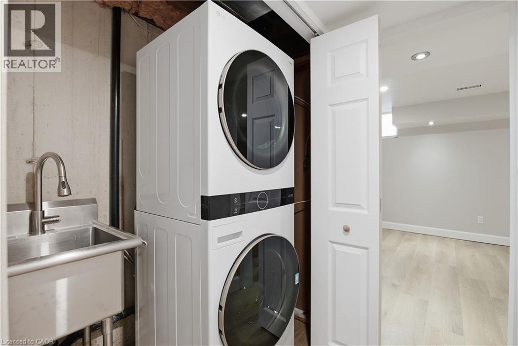 Stacked laundry appliances, stainless steel utility sink with gooseneck faucet, light wood-finish flooring, and recessed ceiling lighting - 30 S Imperial Road Unit# 3, Guelph, ON