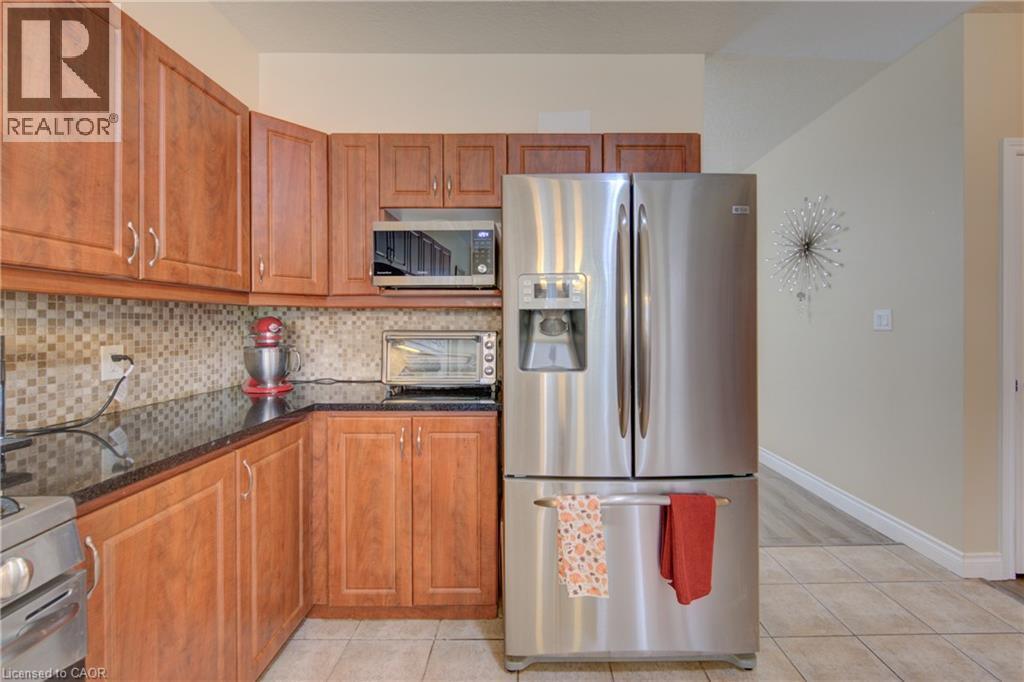 Kitchen featuring cabinetry, dark countertops, a tiled backsplash, and light tile flooring - 78 Stuckey Avenue, Baden, ON