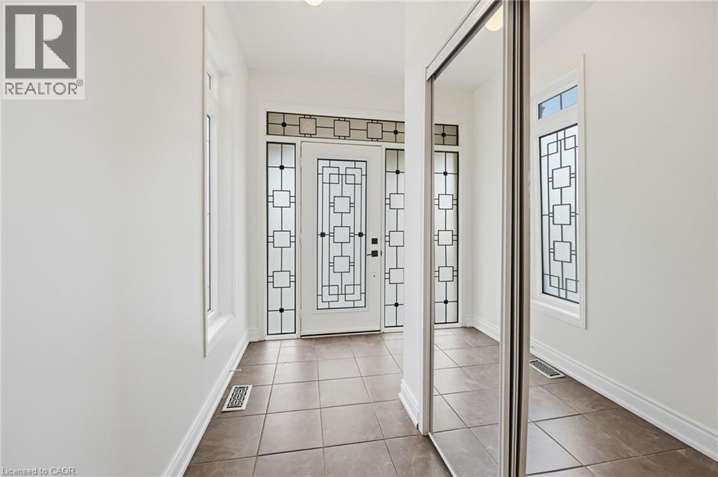 Foyer with tiled flooring, a decorative front entry door, two sidelight windows, and mirrored sliding closet doors - 3198 Tim Dobbie Drive, Burlington, ON