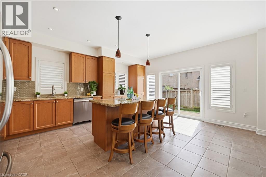 Kitchen featuring shaker-style cabinetry, a central island with countertop seating, stainless steel appliances, and a tiled backsplash - 3198 Tim Dobbie Drive, Burlington, ON