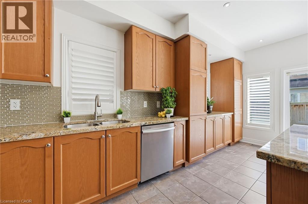 Kitchen featuring extensive wood cabinetry, granite countertops, a tile backsplash, stainless steel appliances, and a double basin sink with a gooseneck faucet - 3198 Tim Dobbie Drive, Burlington, ON