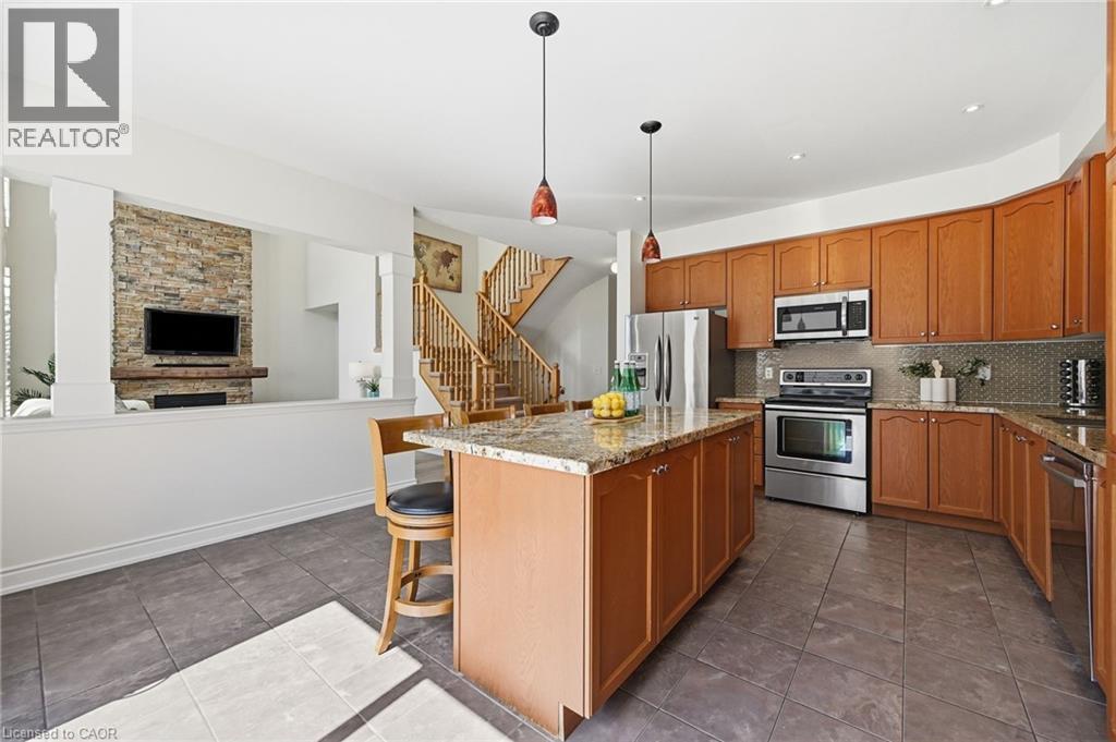 Kitchen featuring a center island with a granite countertop, wood cabinetry, stainless steel appliances, and tile flooring - 3198 Tim Dobbie Drive, Burlington, ON